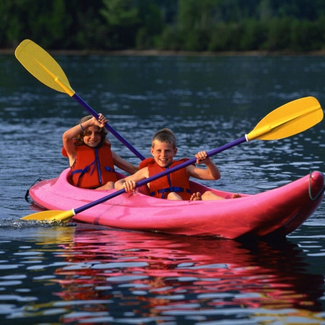 A picture of two children on a red kayak